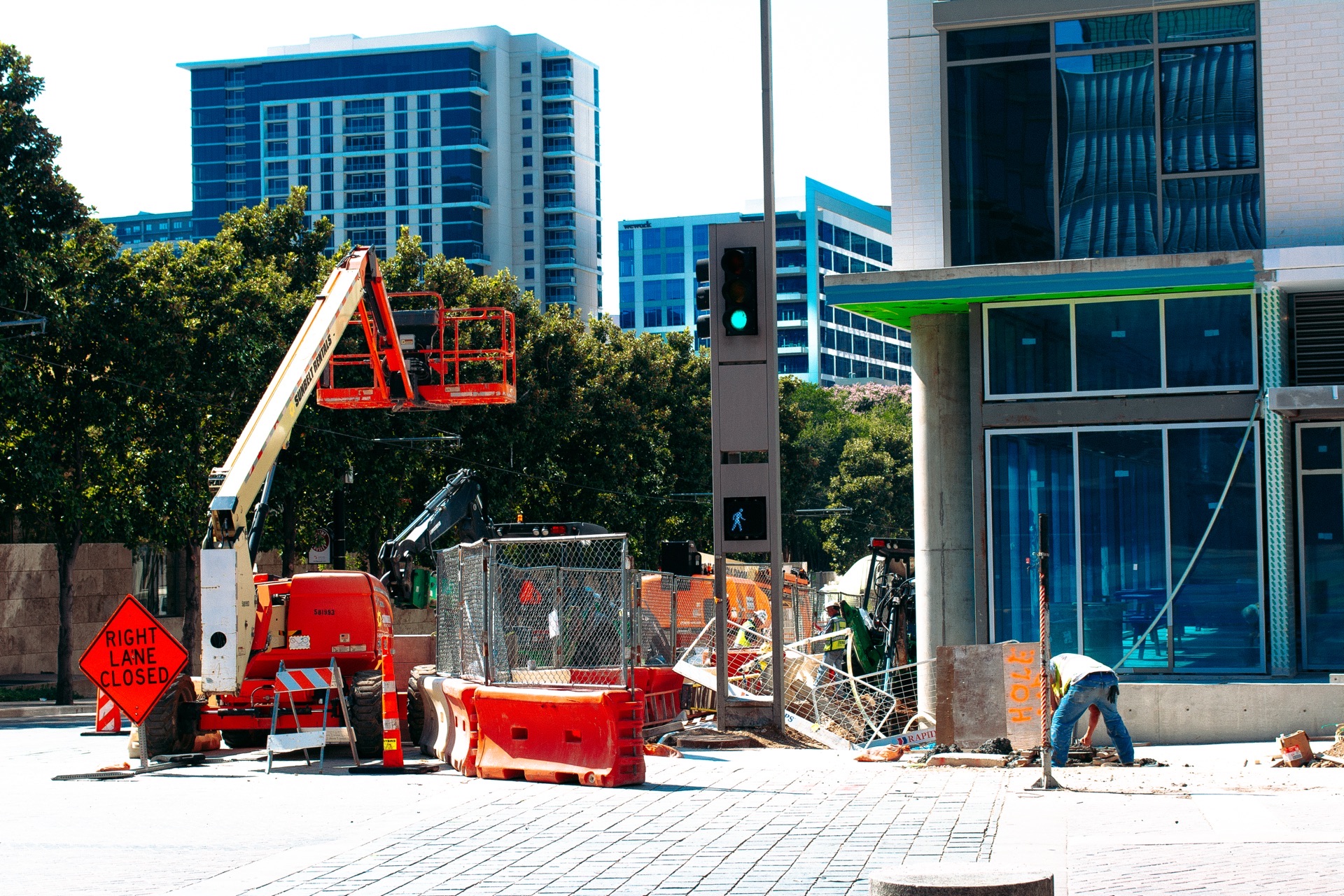 Street construction below glass towers: an orange boom lift, barriers, and a Right Lane Closed sign — from the Aerial study
