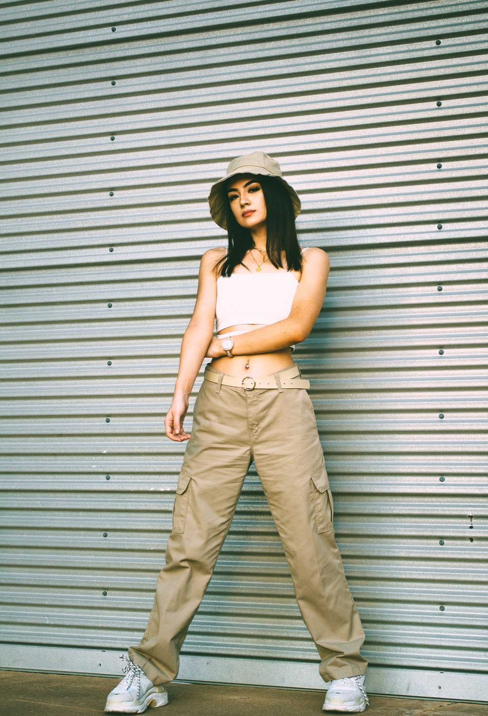 A low-angle, wide-legged stance before corrugated metal, khaki cargos running down to chunky white sneakers — from the BALENCI sequence