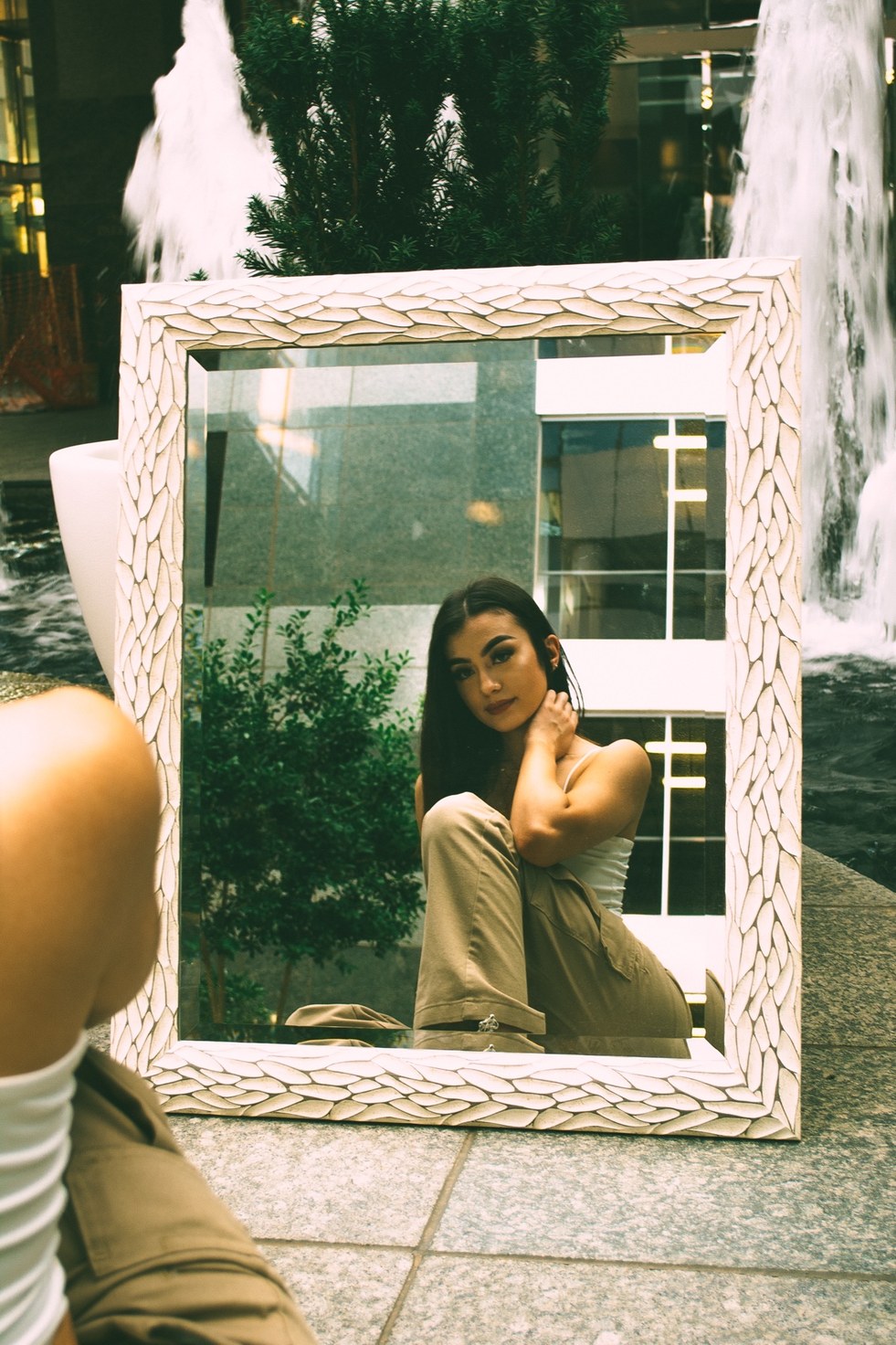 A seated figure reflected in a carved white mirror propped between two courtyard fountains — from the BALENCI sequence