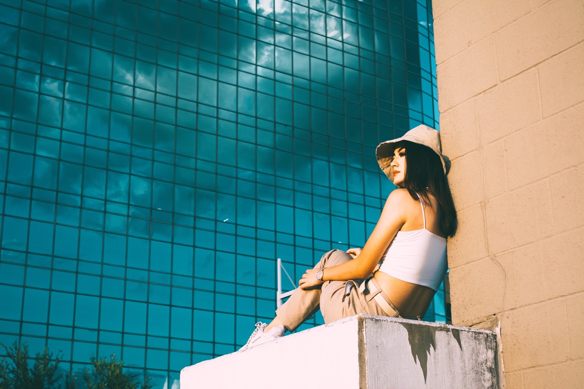 Seated on a concrete ledge against a tan block wall, a blue glass tower rising behind — from the BALENCI sequence