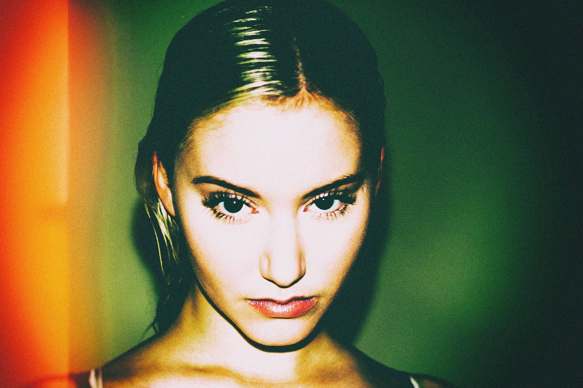 Nocturnal study — a level stare under hard flash, hair slicked back, against green with an edge of orange light