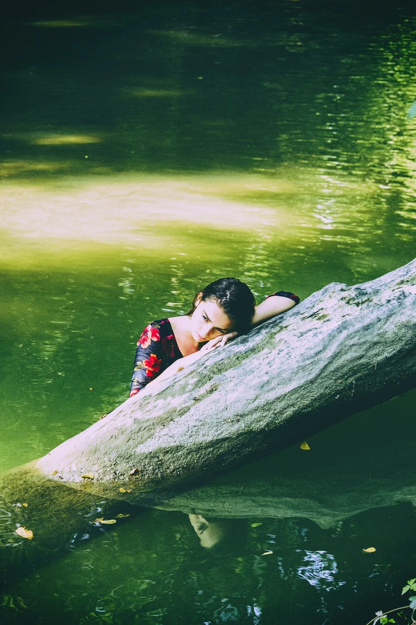 A wet-haired portrait rising from dark green water — Purity study