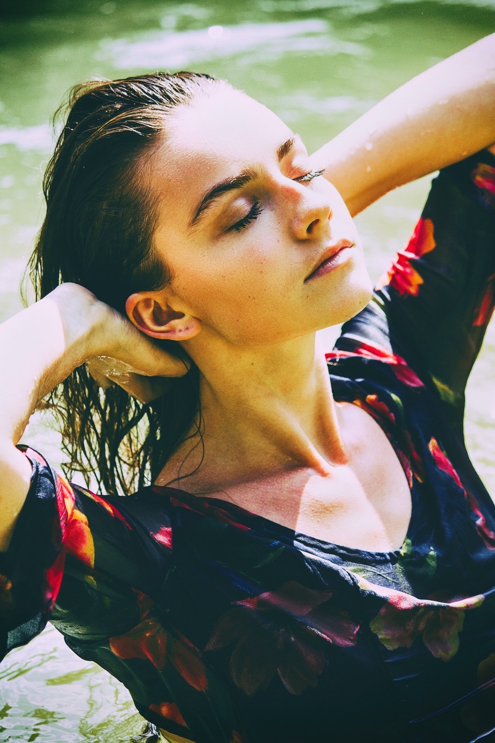 Purity study — eyes closed, hands behind the head, in a floral dress at the water