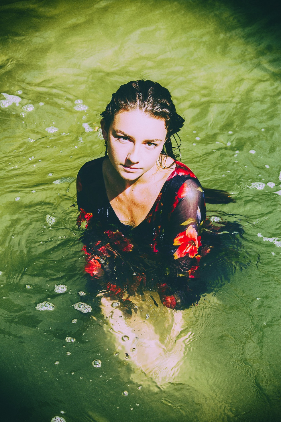 Purity study — seen from above, standing in green water in a floral dress