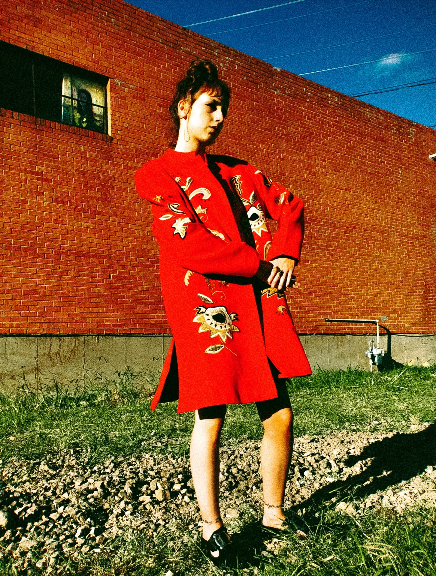 A figure in a sculptural red coat against a brick wall — Rouge study
