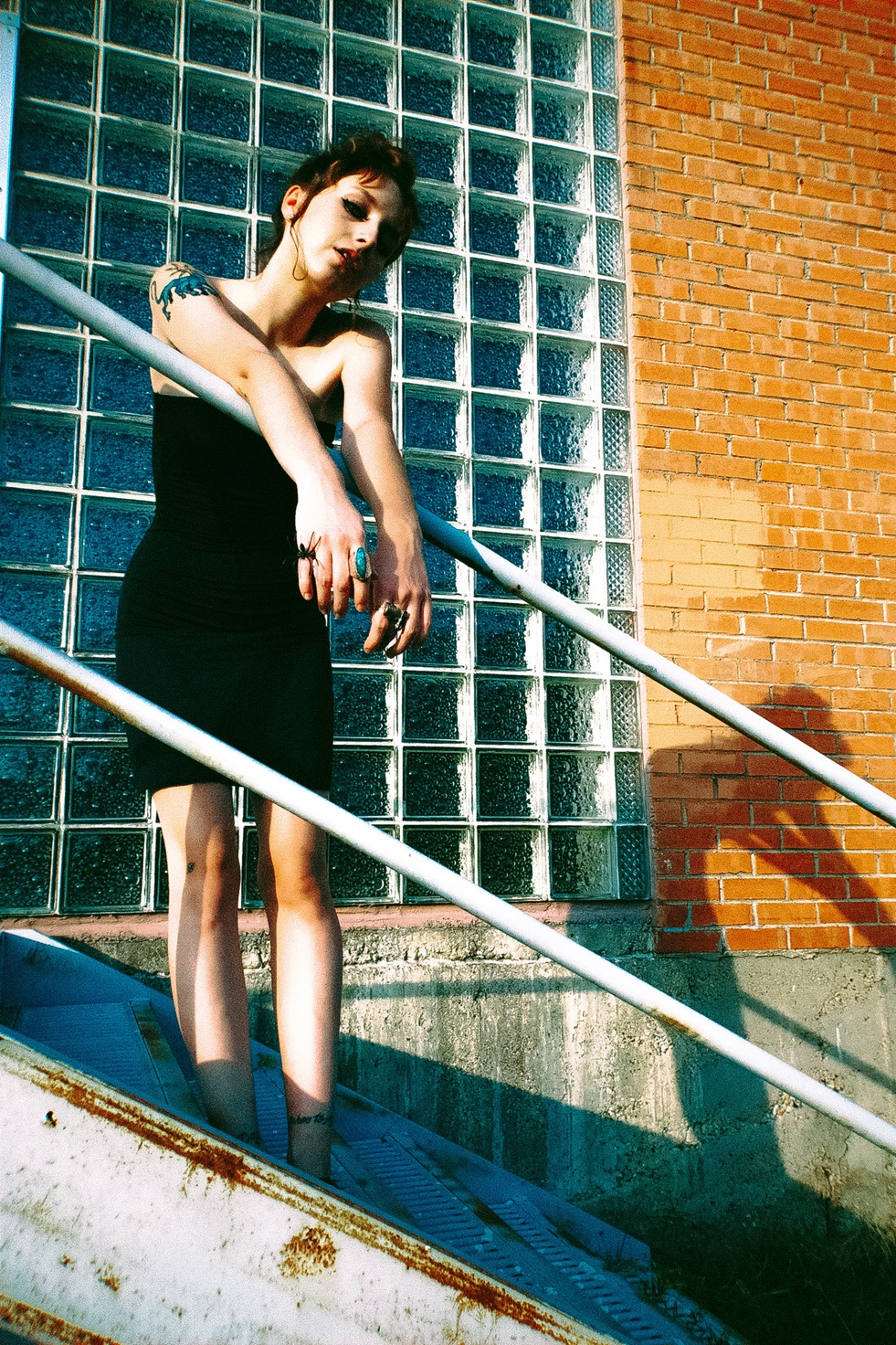 Rouge study — a black dress on a stair rail beside glass block and brick