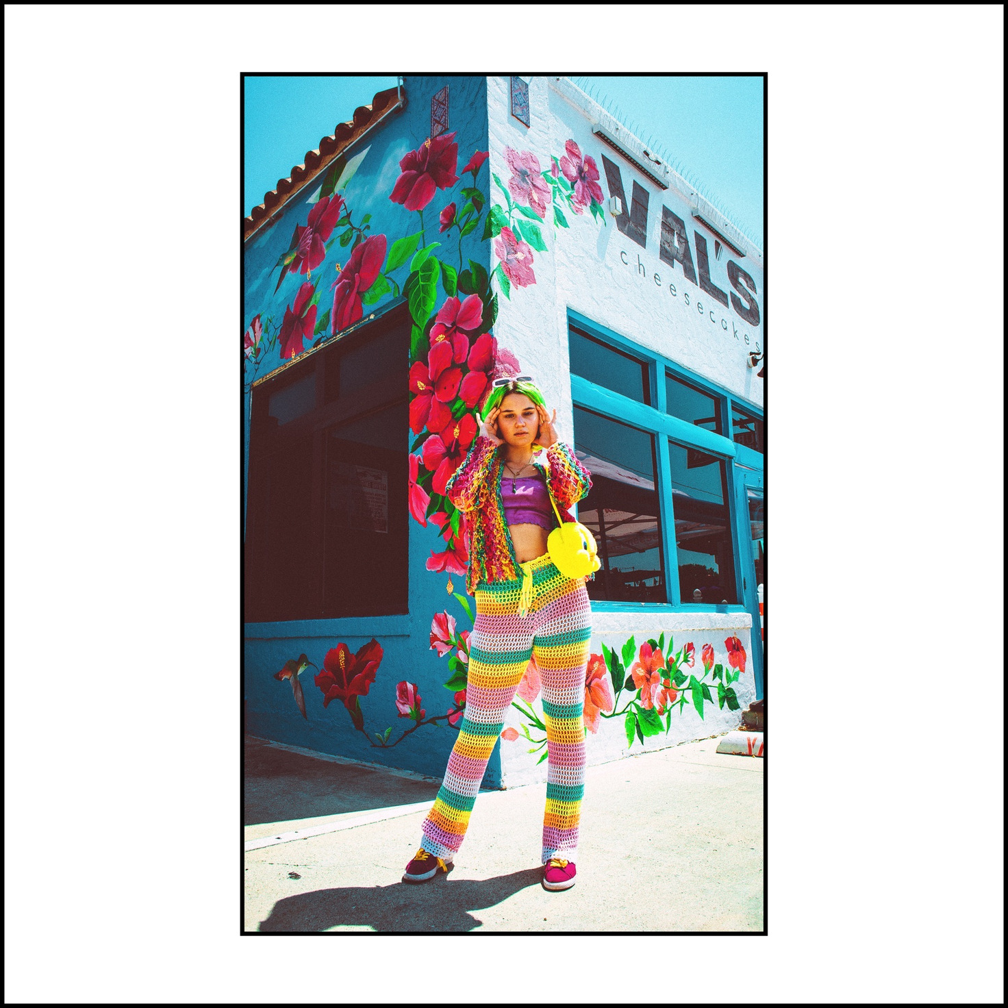 A green-haired model in rainbow crochet stands before a hibiscus mural on a corner storefront — from the STVPID study