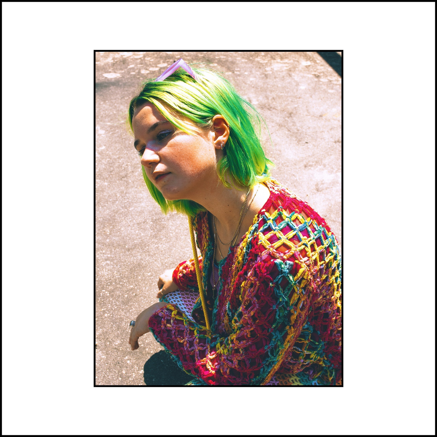 A high-angle close portrait in hard sun, green bob and a rainbow crochet cardigan — from the STVPID study