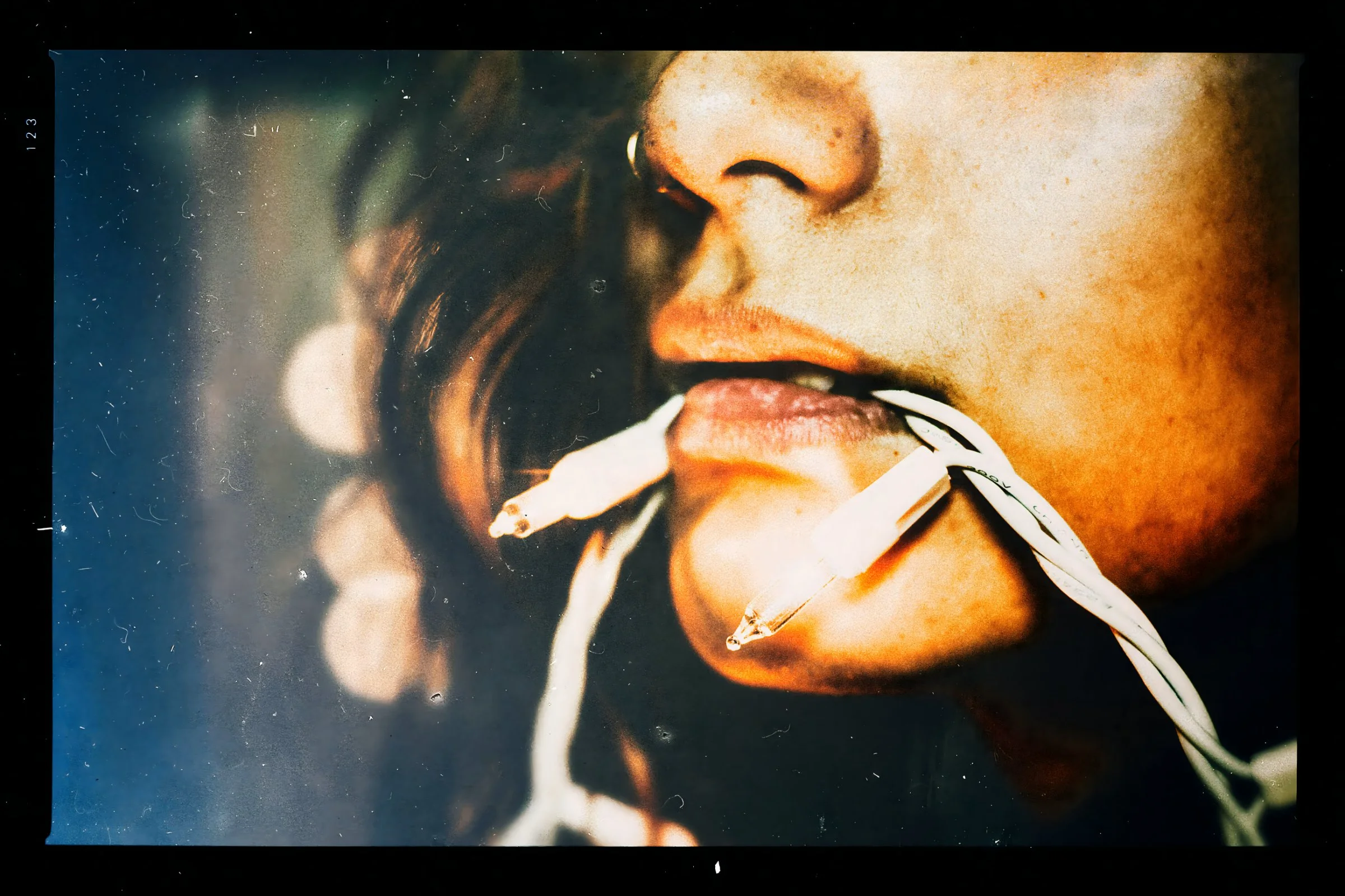 A close crop of a parted mouth holding a white wire of small bulbs, printed with its black film border — the Trance study