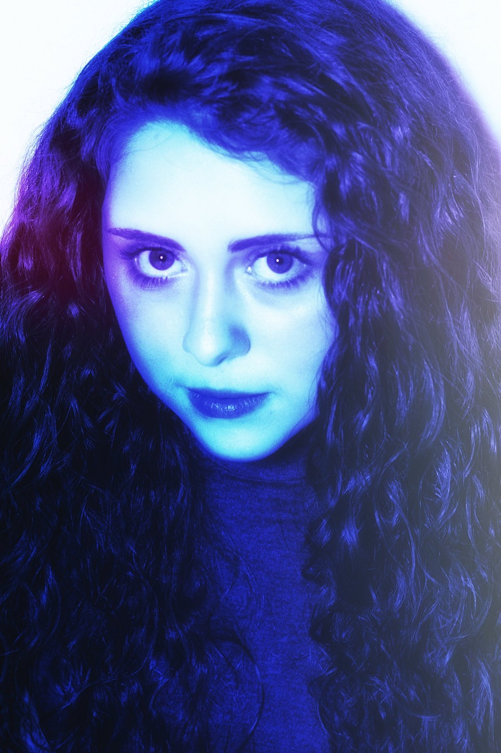 A direct blue-lit portrait framed by long dark curls