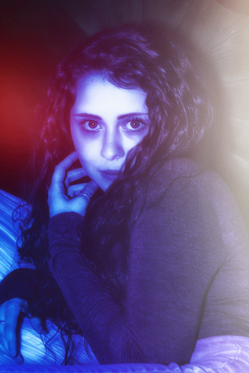 A seated portrait between red and blue light, hand at the collar