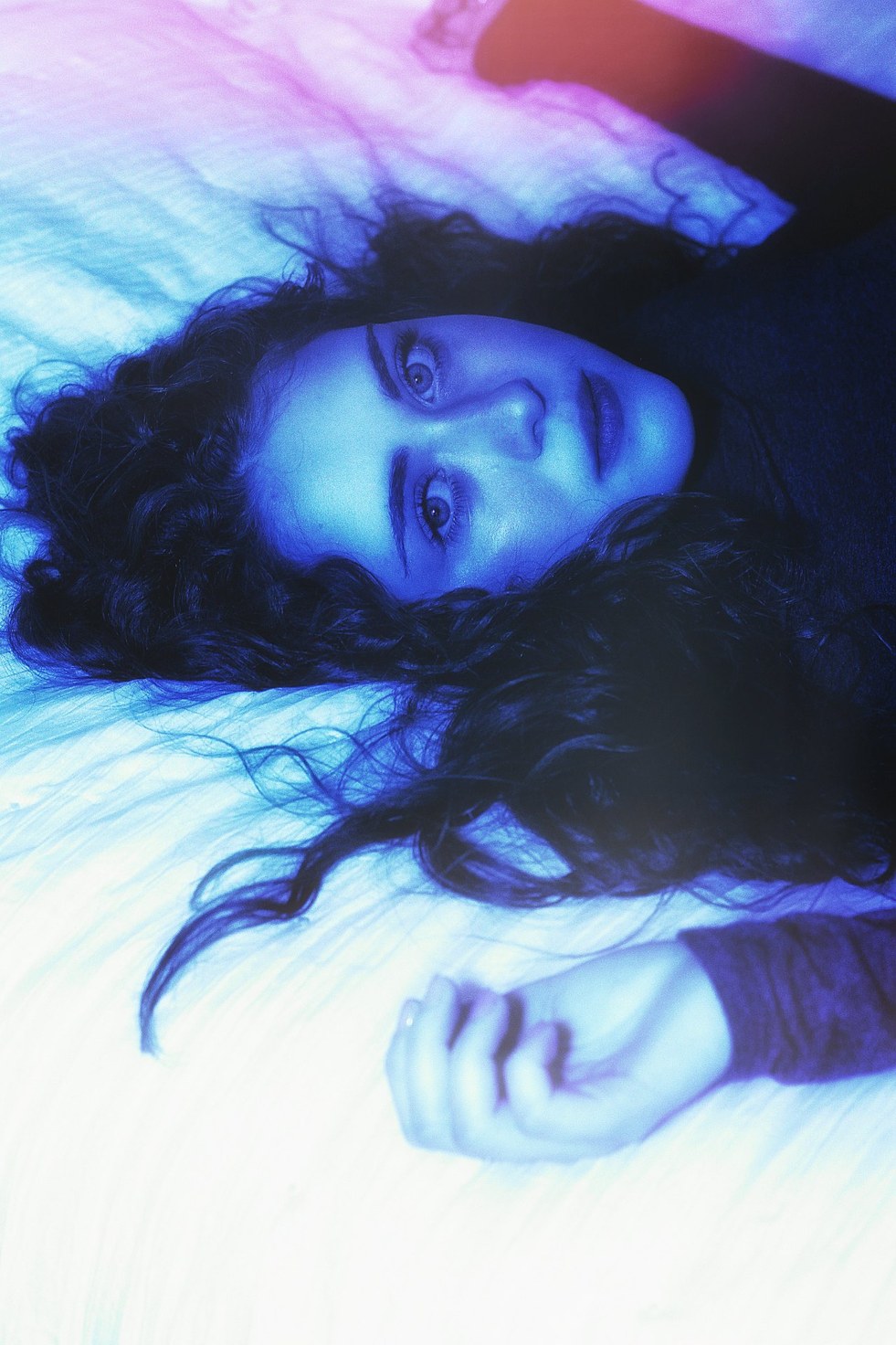 A reclining portrait under violet light, eyes to the camera