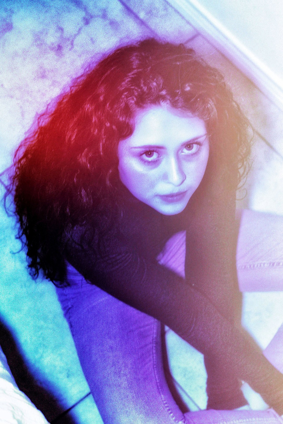 A seated portrait looking up, red light through dark curls